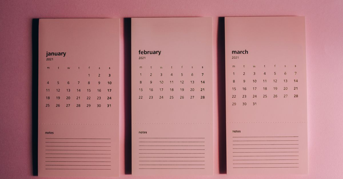 Overhead view of modern paper calendars with horizontal lines for notes and monthly dates on pink background